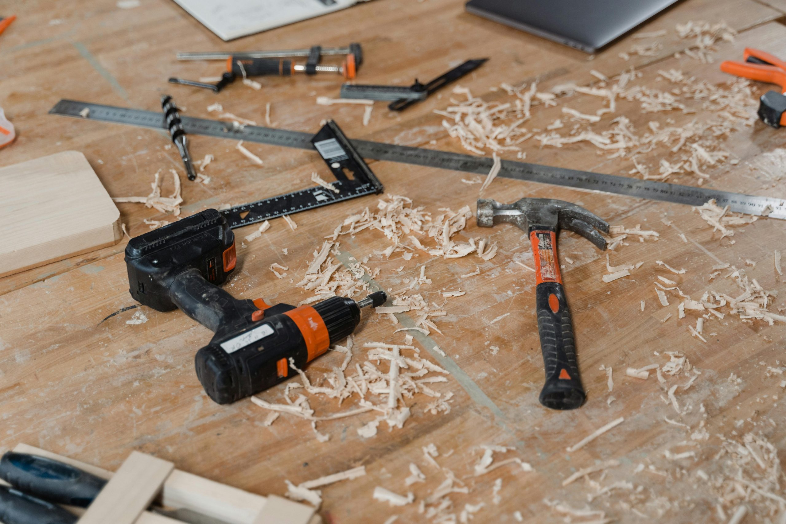 drill, hammer, and other tools on a woodworking table with wood shavings